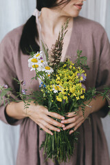 Stylish woman in linen dress holding wildflowers bouquet at pastel fabric. Simple slow living