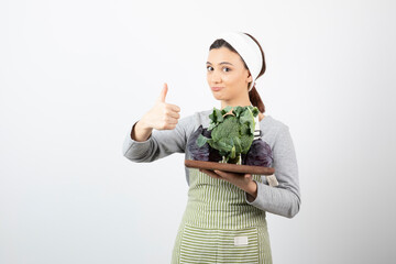 Shot of young cook holding plate of cabbage and broccoli and giving thumbs up