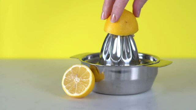 A metal lemon squeezer on a white surface and with a vibrant yellow background. Lemon being pressed and juice squeezed out in real time with fruit in foreground. Healthy food concept footage.