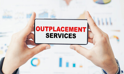 Closeup on businessman holding a smartphone with text OUTPLACEMENT SERVICES.