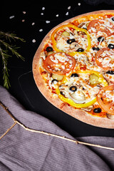 pizza on black textured background with dark napkin and golden sprigs