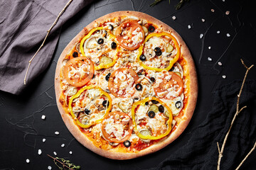 pizza on black textured background with dark napkin and golden sprigs top view