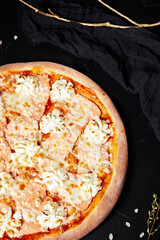pizza on black textured background with dark napkin and golden sprigs