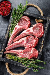 Raw lamb meat chops steaks in a wooden tray. Black background. Top view