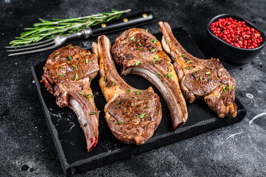 Barbecue fried lamb meat chops on a marble board. Black background. Top view