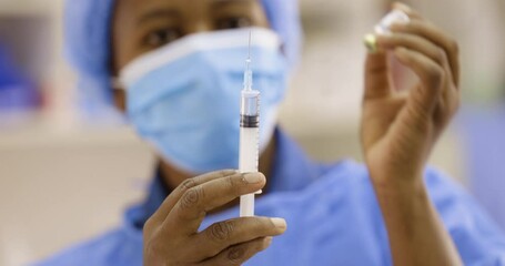 Black African female doctor nurse pulling Covid-19 vaccine liquid from vial