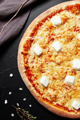 pizza on black textured background with dark napkin and golden sprigs top view