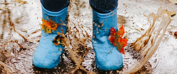 Teenager girl wearing blue rain boots jumping into a puddle on rainy autumn day. Closeup. Banner.	