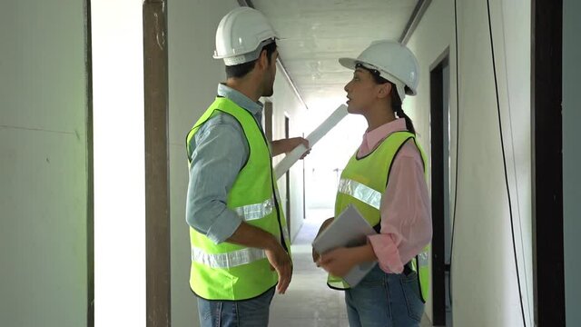 Builder caucasian ,asian contractor, engineer man and woman greeting handshake, discussing, inspecting, wearing safety helmets in construction building, apartment at site. Industrial teamwork concept.