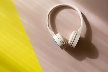 White wireless headphones over colourful yellow pink background with copy space.