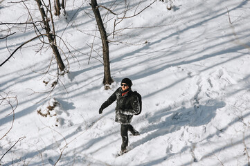 A young man, a wanderer, a tourist in black clothes with a backpack on his back walks through the snowy forest, enjoying the beautiful nature and fresh air. Photography, concept.