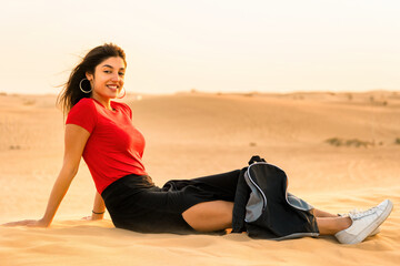 Fototapeta na wymiar A girl in a red T-shirt and backpack is resting on the desert sand. Perfect shot for travel and vacations.
