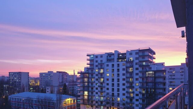 Balcony view of a city sunset. Day to night timelapse in urban area with buildings and pink sky.