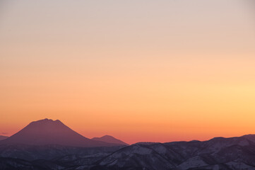 Fototapeta na wymiar オレンジ色の夕暮れの空と山並みのシルエット。