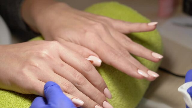 Closeup view 4k video footage of professional manicurist applying wet cleanser to woman's nails using white cotton pad. End of manicure and polishing procedures