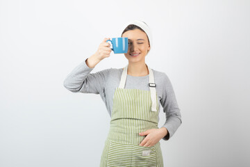 Image of a pretty young woman in apron covering an eye with a blue cup