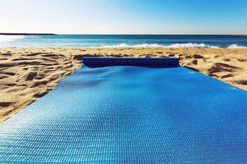Blue yoga mat is on a sandy beach by the sea. Barcelona, Spain