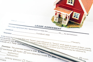 Lease agreement contract form with tiny red model house and pen.
