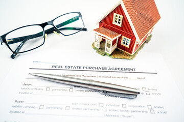 Real estate purchase agreement contract with tiny red model house, glasses and pen for props.