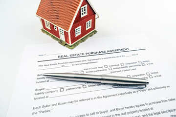 Real estate purchase agreement contract with tiny red model house and pen for props.