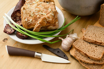 baked meat and blood sausage on a plate, green onion and garlic on wooden background, home cooking