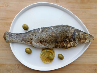 grilled sea bass with lemon, onion, herbs on a large white plate.