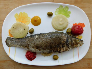 grilled sea bass with lemon, onion, herbs on a large white plate.