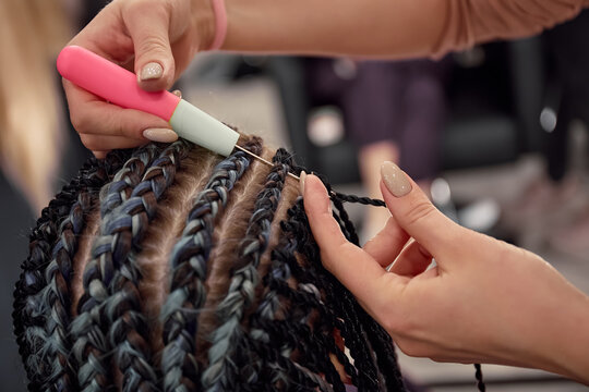 The hairdresser braids the girl in afro-braids in the beauty salon. Close-up