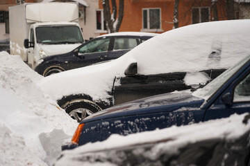 Cars stand along the street covered with snow. Cars under the snow during a heavy snowfall.