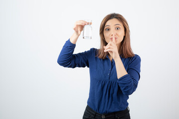 Young woman in blue blouse holding water and giving silence sign