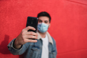 Chico joven atractivo sobre pared roja usando smartphone