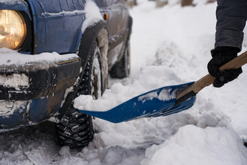 The guy is holding a shovel in his hands with snow near the car. Clearing a road for a car during a snowfall