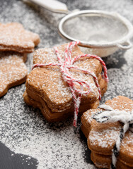 Star shaped baked gingerbread cookies sprinkled with powdered sugar on a black table