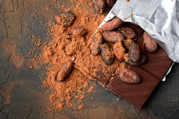 Dark chocolate, cocoa beans and powder on a dark stone background.