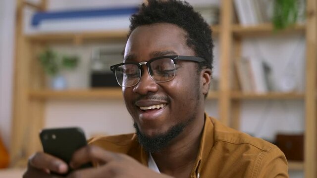 Man read funny news on social media or get text message and laugh Spbas. Hipster black afro guy at home office in glasses resting and using app in smartphone for entertainment. Concept content, enjoy