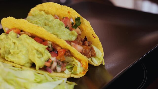 Woman hands placing hard shell tacos on serving plate, camera slide, extrs close up