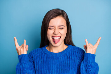 Portrait of young happy crazy excited positive girl stick tongue out showing rock n roll sign isolated on blue color background