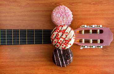 Artistic food composition of donuts on top of a acoustic guitar. Top view. Colorful cakes with sprinkles. Wood background.