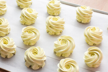 Many sweet handmade zephyrs or marshmallows drying on baking sheet covered with white parchment. Cooking concept. Isolated close-up of white marshmallows, meringues, zephyrs. Sweet delicious desserts.