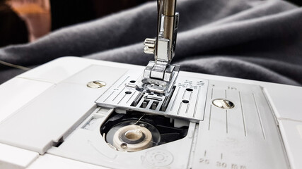 a sewing machine foot and a gray cloth in the background. the work of a seamstress.