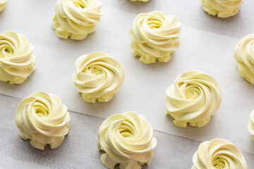 Many sweet handmade zephyrs or marshmallows drying on baking sheet covered with white parchment. Cooking concept. Isolated close-up of white marshmallows, meringues, zephyrs. Sweet delicious desserts.