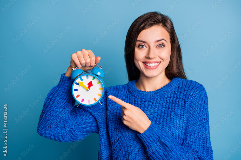 Sticker Photo of young happy cheerful good mood positive girl smiling pointing finger on clock isolated on blue color background