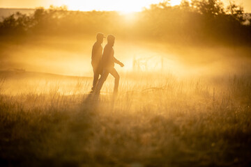 Two people walking through the grass one early morning in winter with the sun coming up in the distance.