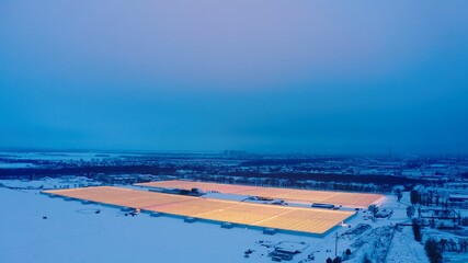 Aerial side view of large industrial greenhouses for growing plants in winter. light pollution. winter day at sunset. Flying along modern plantation glasshouse area. growing plants vegetables flowers