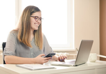  young woman working from home using smart phone and computer, woman's hands using smart phone in interior, at home workplace using technology, credit card