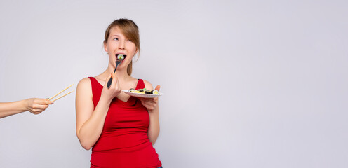 Banner, grey background. The young beautiful caucasian girl eats sushi using a fork with crooked...