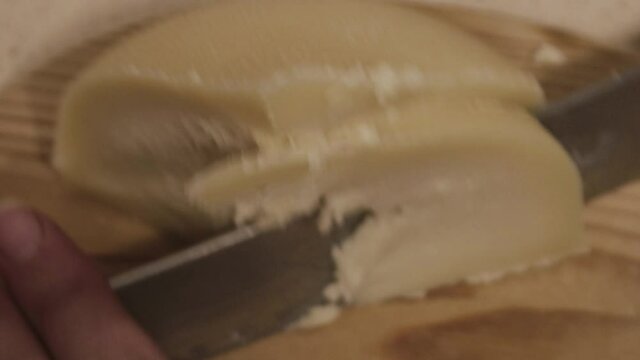 Galician tetilla cheese is cut with a knife by a woman's hands in a kitchen.