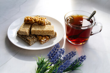 Black tea in a glass mug, a plate with healthy handmade oriental sweets, nuts, seeds and sesame seeds in caramel sugar. Sunny morning, tea party.
