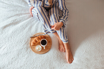 women's beautiful legs in pajamas and next to a coffee with a croissant.the concept of coffee in...