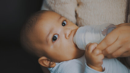 Close up adorable dark skin baby drinking his milk from the bottle in mothers hands. High quality photo